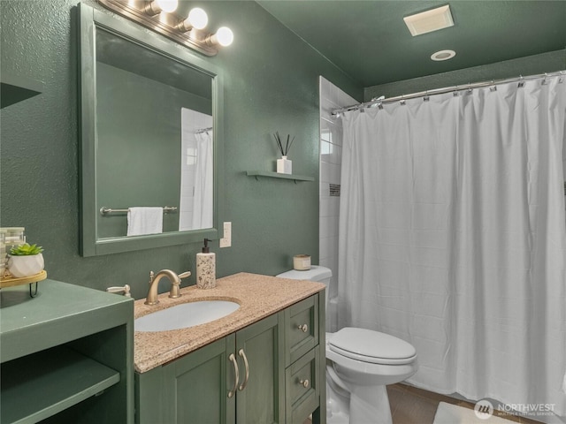 full bathroom featuring vanity, a textured wall, and toilet