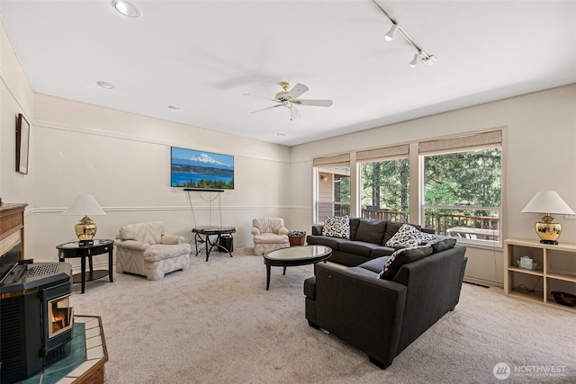 carpeted living room with track lighting, a ceiling fan, and a wood stove