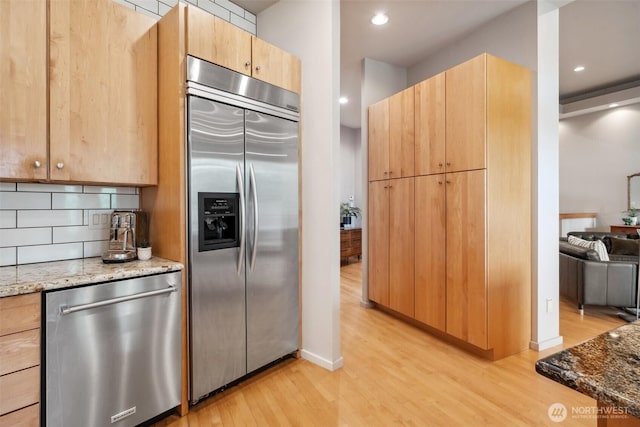 kitchen featuring appliances with stainless steel finishes, light stone countertops, and light wood-type flooring