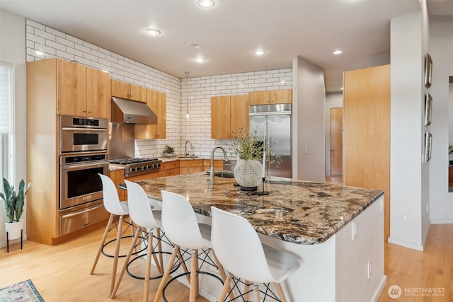 kitchen with a breakfast bar, under cabinet range hood, a sink, a warming drawer, and stainless steel appliances
