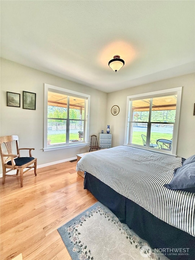 bedroom with baseboards, multiple windows, and light wood-style flooring