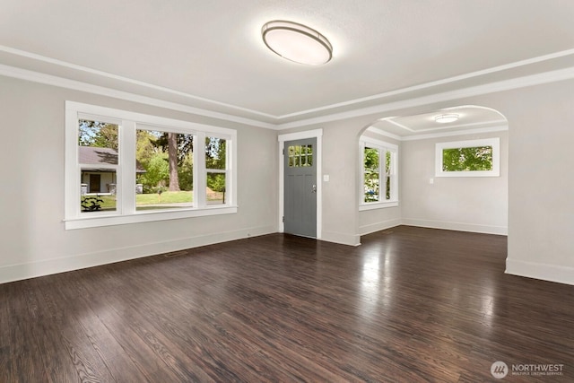 unfurnished room featuring arched walkways, baseboards, wood finished floors, and crown molding