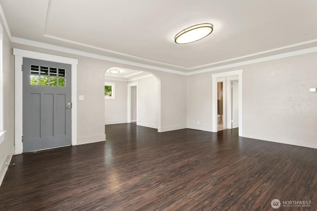 unfurnished living room with arched walkways, wood finished floors, crown molding, and baseboards