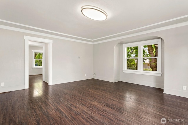 empty room with wood finished floors, arched walkways, baseboards, and crown molding