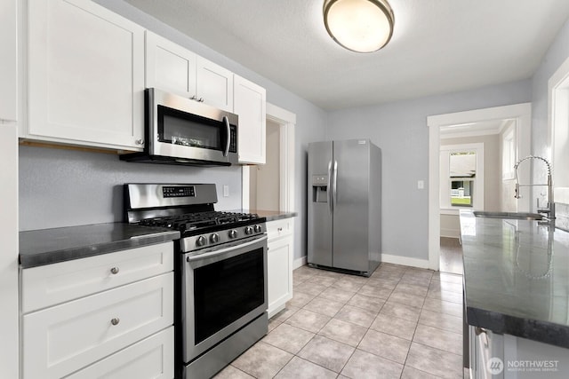 kitchen featuring stainless steel appliances, a sink, white cabinets, light tile patterned floors, and baseboards
