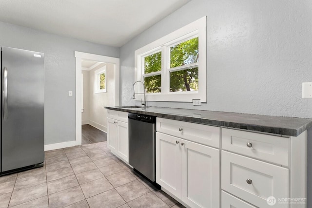 kitchen with stainless steel appliances, a sink, white cabinets, light tile patterned floors, and baseboards