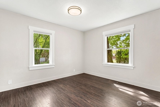 spare room featuring plenty of natural light, baseboards, dark wood finished floors, and crown molding