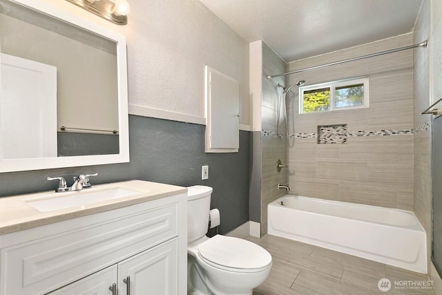 bathroom featuring toilet, bathtub / shower combination, vanity, and a textured wall