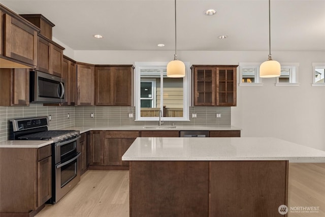 kitchen featuring backsplash, appliances with stainless steel finishes, a sink, light stone counters, and light wood-style floors