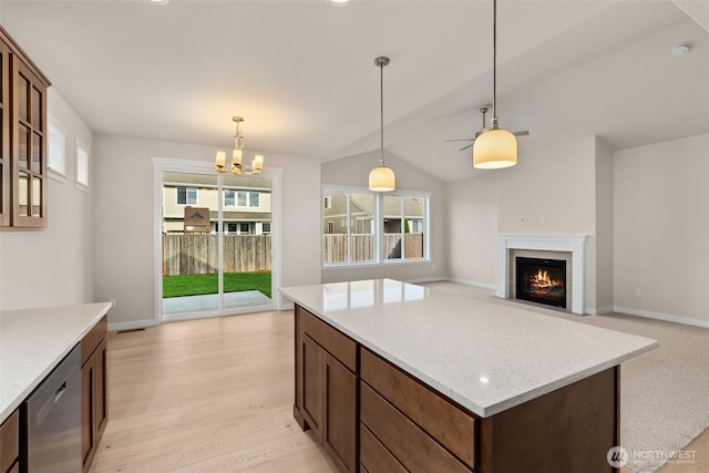 kitchen with stainless steel dishwasher, a kitchen island, a fireplace with flush hearth, light wood finished floors, and hanging light fixtures