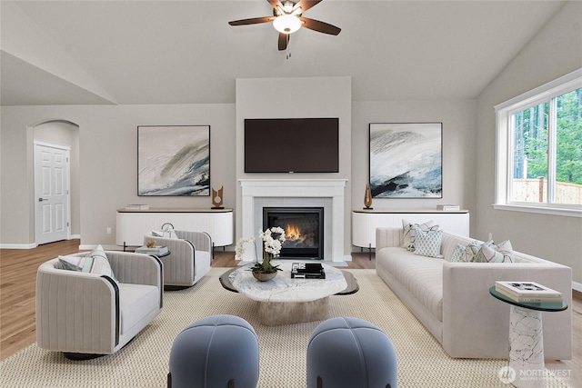 living area featuring ceiling fan, baseboards, a fireplace with flush hearth, wood finished floors, and vaulted ceiling