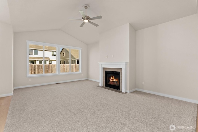 unfurnished living room featuring ceiling fan, a fireplace with flush hearth, vaulted ceiling, baseboards, and carpet flooring
