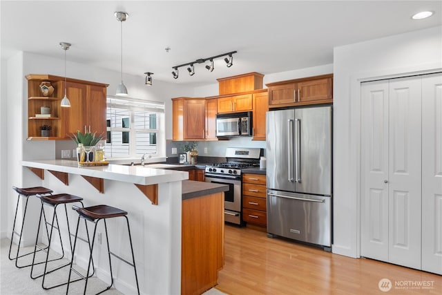 kitchen with a peninsula, a kitchen breakfast bar, brown cabinets, appliances with stainless steel finishes, and hanging light fixtures