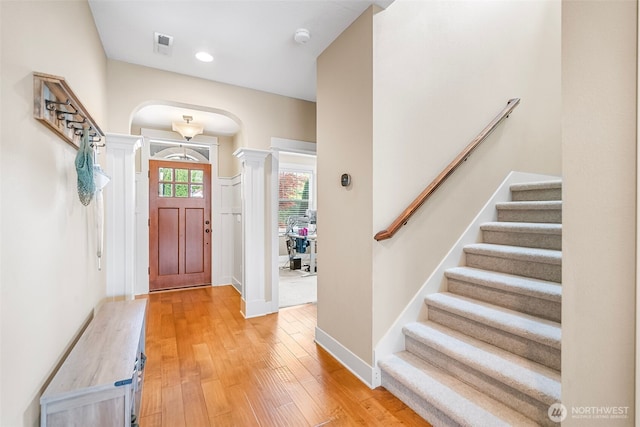 foyer featuring visible vents, stairs, ornate columns, arched walkways, and light wood finished floors