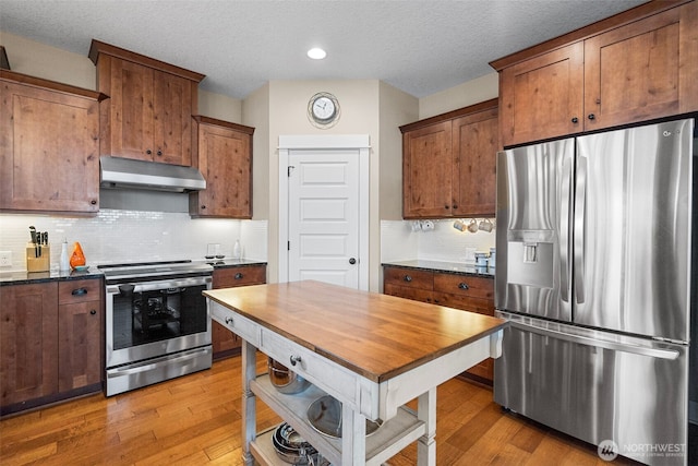 kitchen with appliances with stainless steel finishes, a textured ceiling, light wood-type flooring, tasteful backsplash, and under cabinet range hood