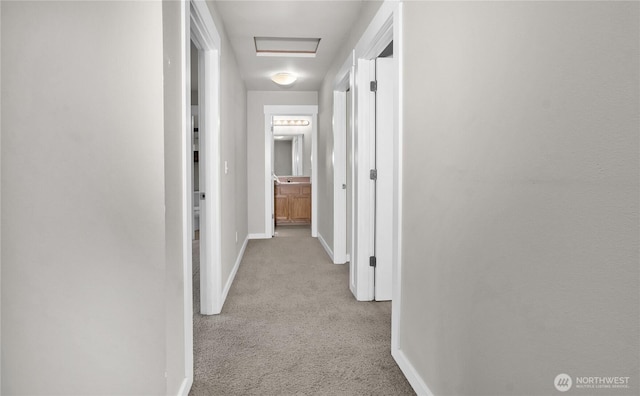 hall featuring carpet floors, baseboards, and attic access