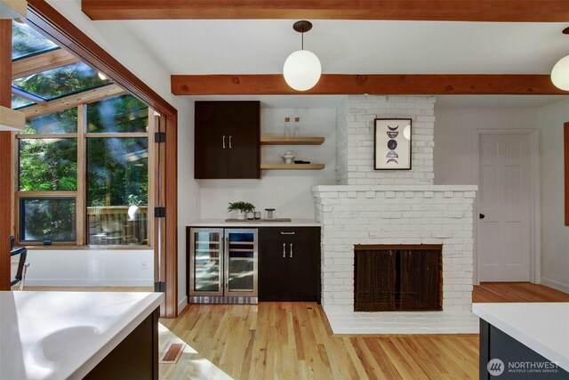 bar featuring wine cooler, beam ceiling, light wood-style floors, hanging light fixtures, and a brick fireplace