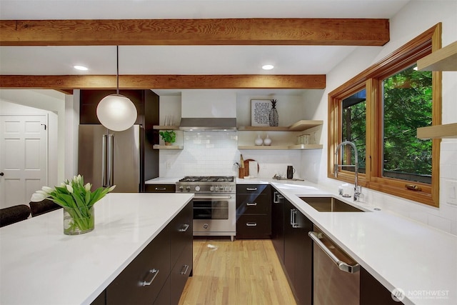 kitchen featuring open shelves, high quality appliances, wall chimney range hood, beamed ceiling, and a sink