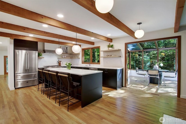kitchen with high end refrigerator, open shelves, light countertops, a kitchen bar, and light wood-style flooring