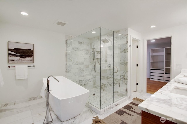 bathroom featuring a freestanding tub, a marble finish shower, double vanity, recessed lighting, and a walk in closet