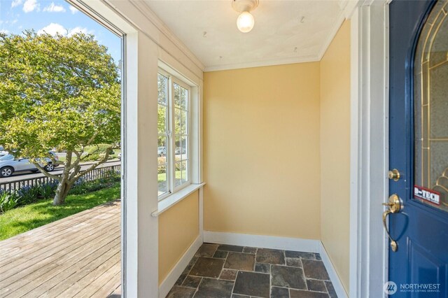 doorway to outside featuring stone tile floors, crown molding, and baseboards