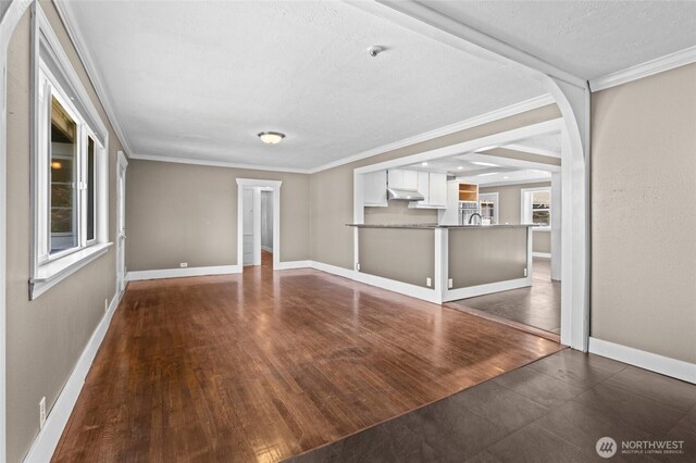 unfurnished living room featuring crown molding, baseboards, and wood finished floors