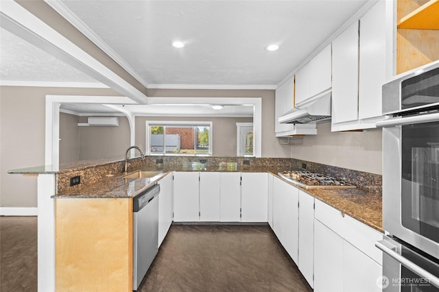 kitchen with a sink, dark stone counters, stainless steel appliances, a peninsula, and ornamental molding