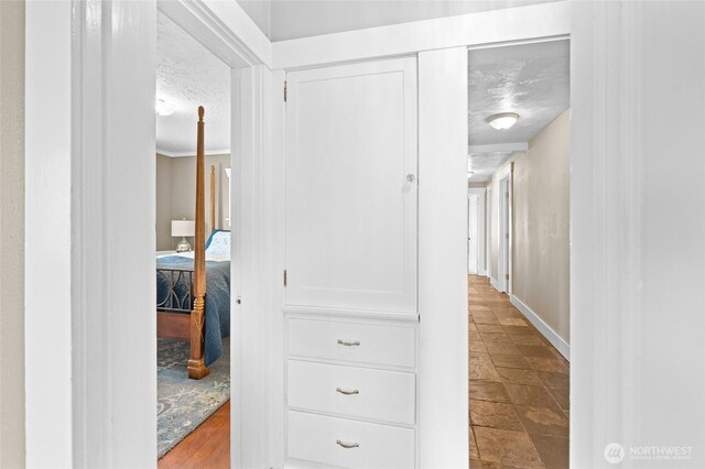 hallway with baseboards, stone finish flooring, and a textured ceiling