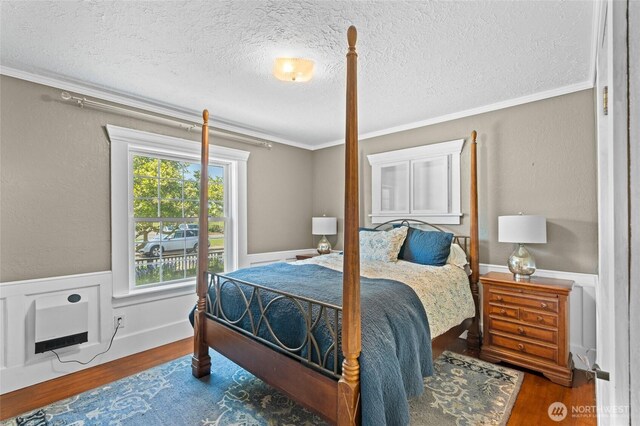 bedroom featuring a textured ceiling, ornamental molding, wood finished floors, and a wainscoted wall
