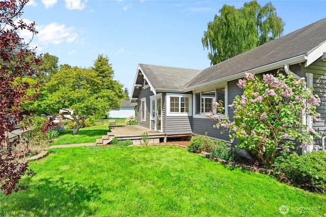 view of property exterior with a lawn, a shingled roof, and a wooden deck