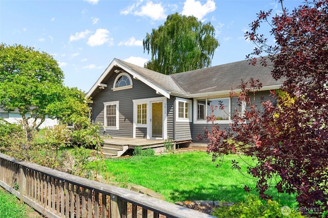 back of house featuring roof with shingles, a yard, and a deck