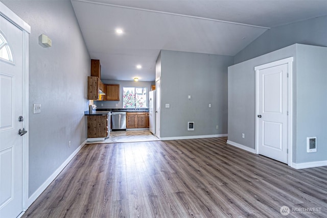 unfurnished living room featuring visible vents, vaulted ceiling, wood finished floors, a sink, and baseboards