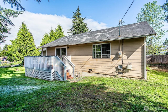 back of house featuring a lawn, fence, a wooden deck, and a shingled roof