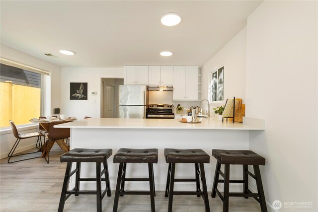 kitchen featuring a peninsula, white cabinetry, under cabinet range hood, a sink, and appliances with stainless steel finishes