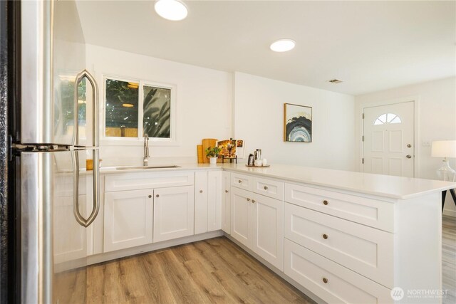 kitchen featuring freestanding refrigerator, a peninsula, a sink, and light wood-style flooring