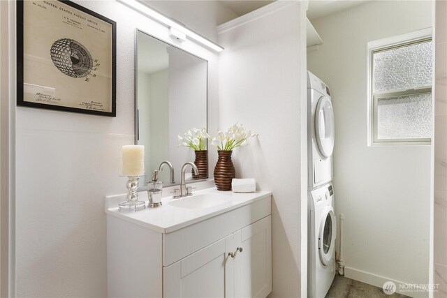 clothes washing area featuring a sink, light wood-style floors, stacked washer and clothes dryer, and laundry area