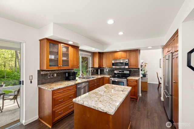 kitchen with appliances with stainless steel finishes, tasteful backsplash, brown cabinets, a sink, and baseboards