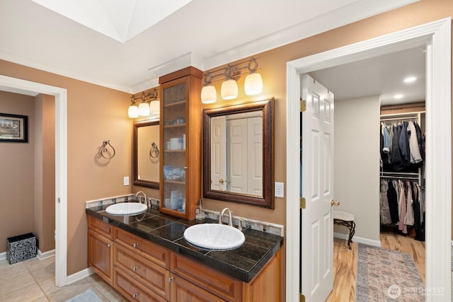 full bath with double vanity, baseboards, a sink, and a walk in closet