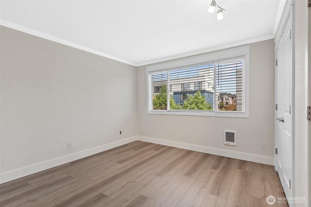 empty room featuring crown molding, baseboards, visible vents, and light wood-type flooring