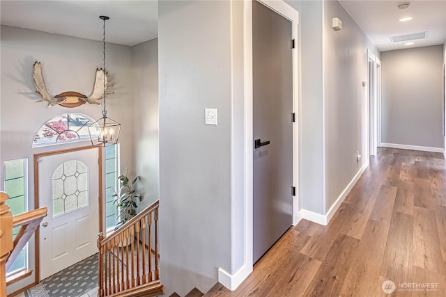 foyer featuring baseboards, a chandelier, wood finished floors, and visible vents