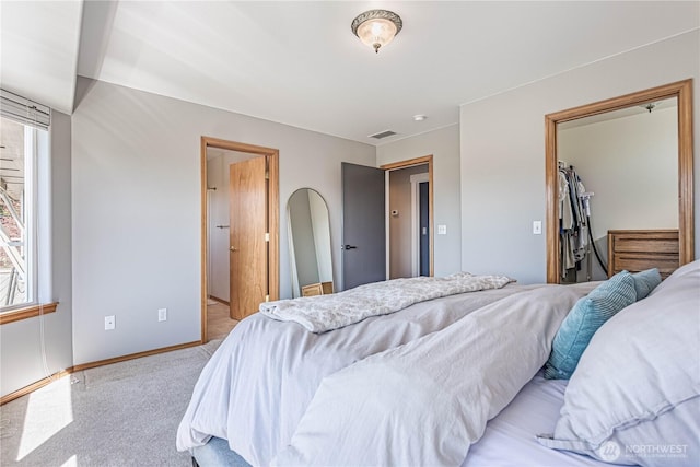 bedroom featuring baseboards, visible vents, a walk in closet, arched walkways, and light carpet