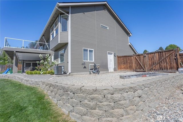 rear view of house with cooling unit, fence, and a gate