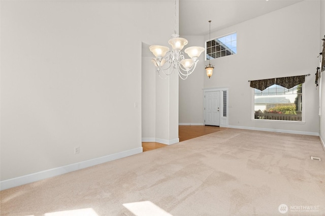 carpeted spare room featuring baseboards, a towering ceiling, and a notable chandelier