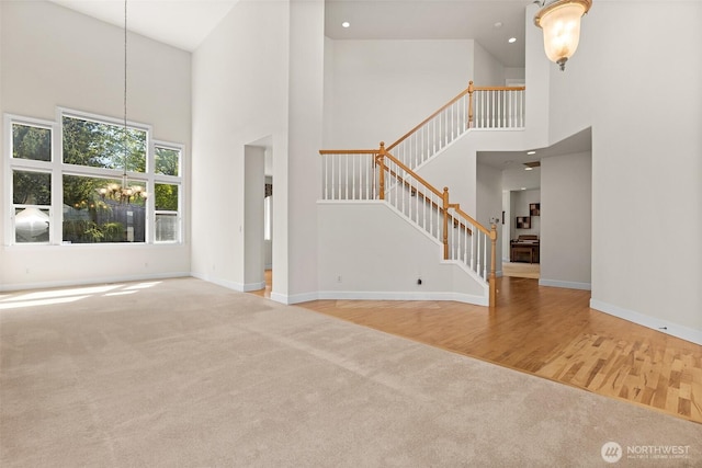 unfurnished living room with a towering ceiling, stairway, carpet floors, baseboards, and an inviting chandelier