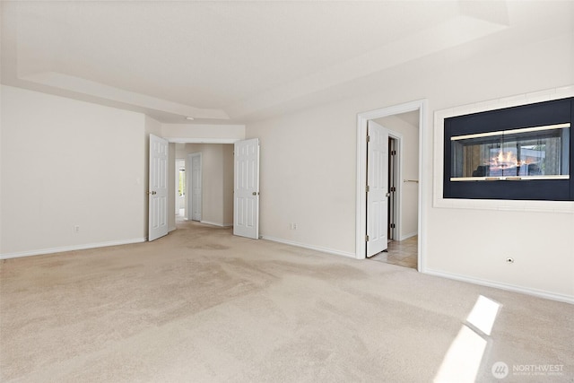 unfurnished room with light colored carpet, a raised ceiling, and baseboards