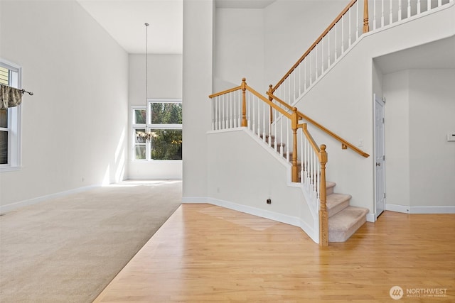 stairway with wood finished floors, a healthy amount of sunlight, and a towering ceiling