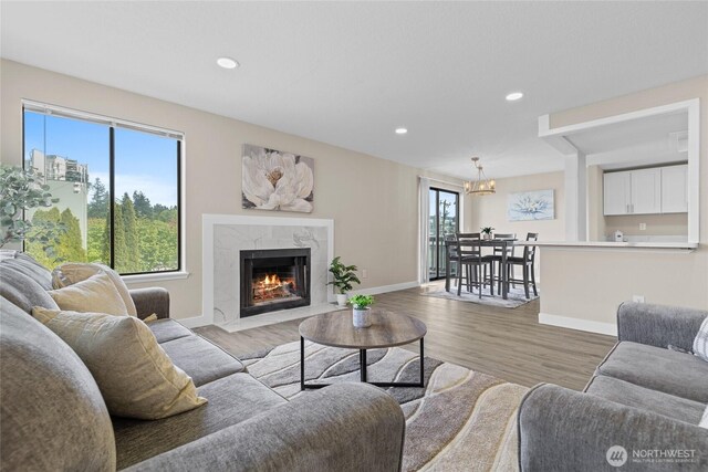living room featuring an inviting chandelier, recessed lighting, baseboards, light wood-type flooring, and a high end fireplace