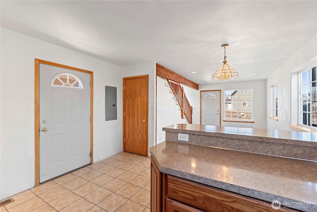 kitchen with electric panel, pendant lighting, dark countertops, brown cabinets, and light tile patterned floors