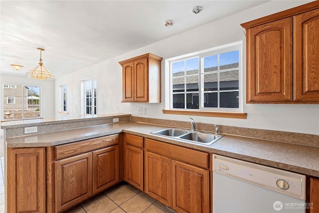 kitchen with brown cabinetry, white dishwasher, a sink, a peninsula, and light tile patterned flooring