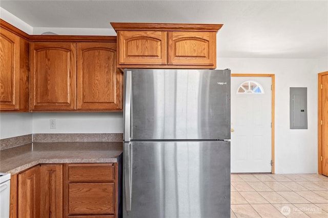 kitchen with brown cabinetry, freestanding refrigerator, light tile patterned floors, and electric panel